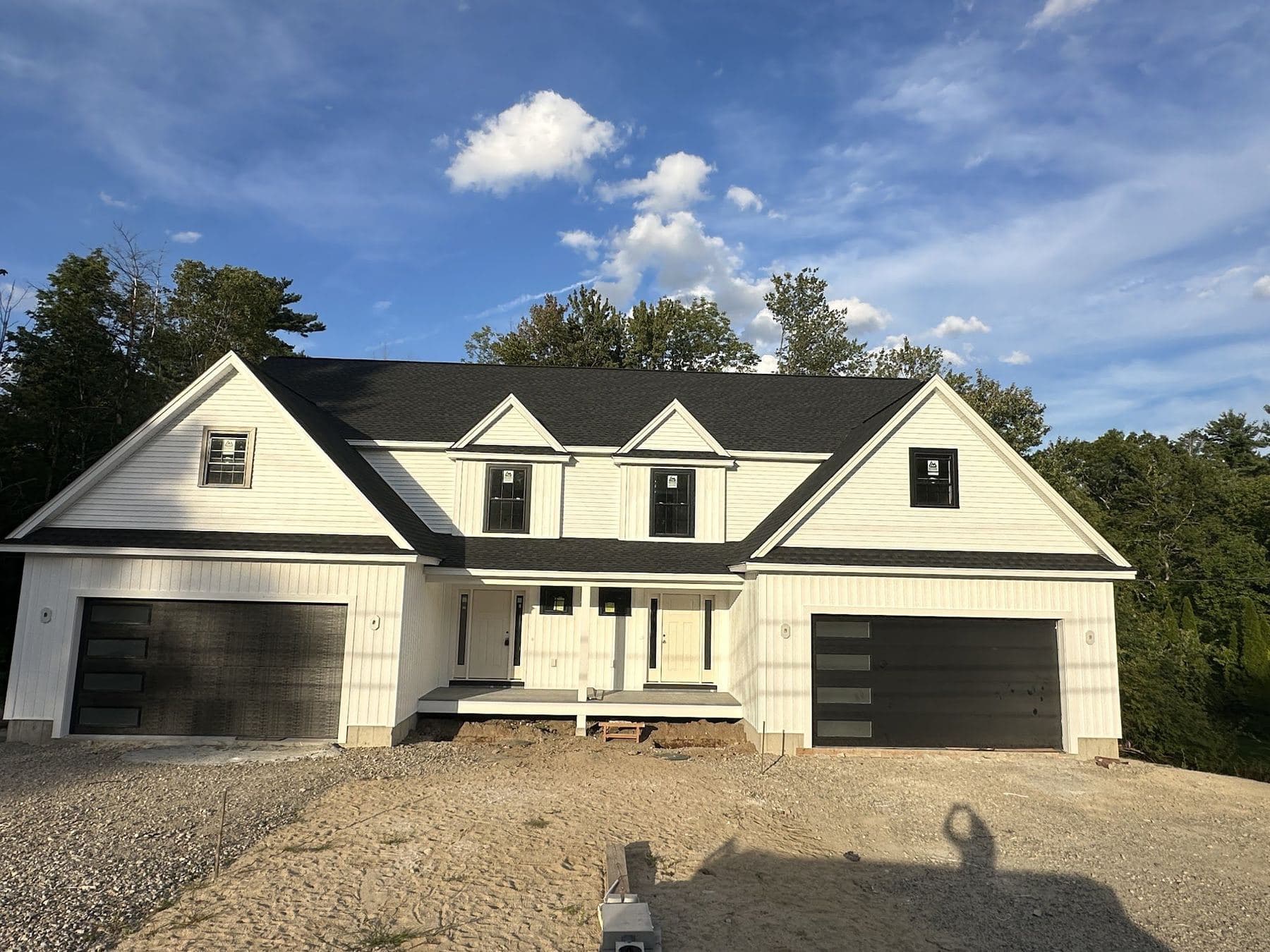 White modern farmhouse with black garage doors in Pelham, NH